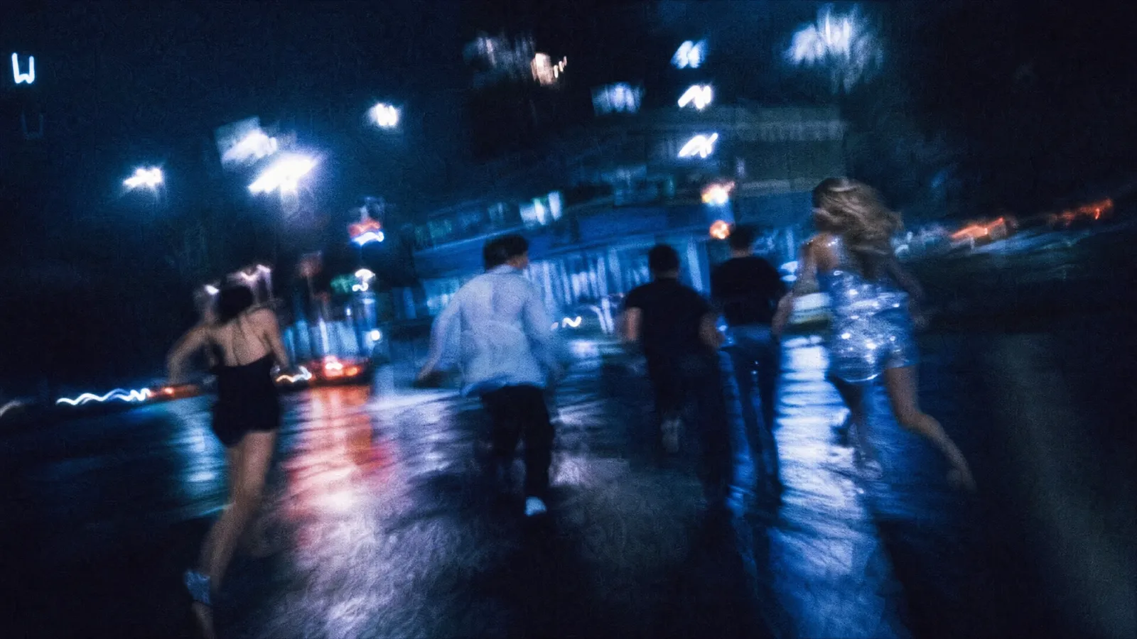 A group of friends crossing a city street at night under the lights